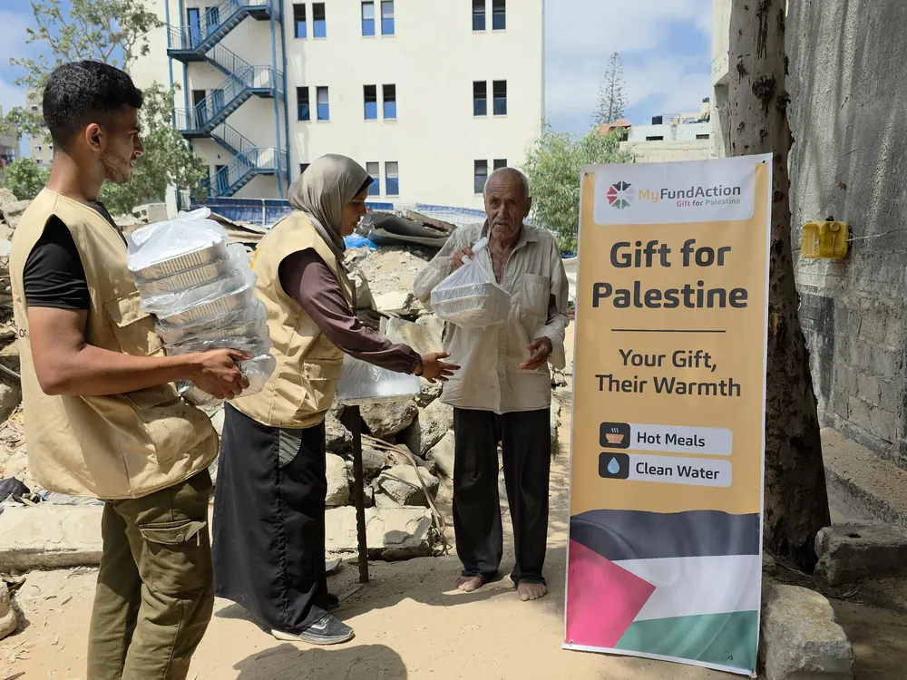 MyFundAction volunteers handing a packed hot meal to an elderly man standing among rubble in Gaza