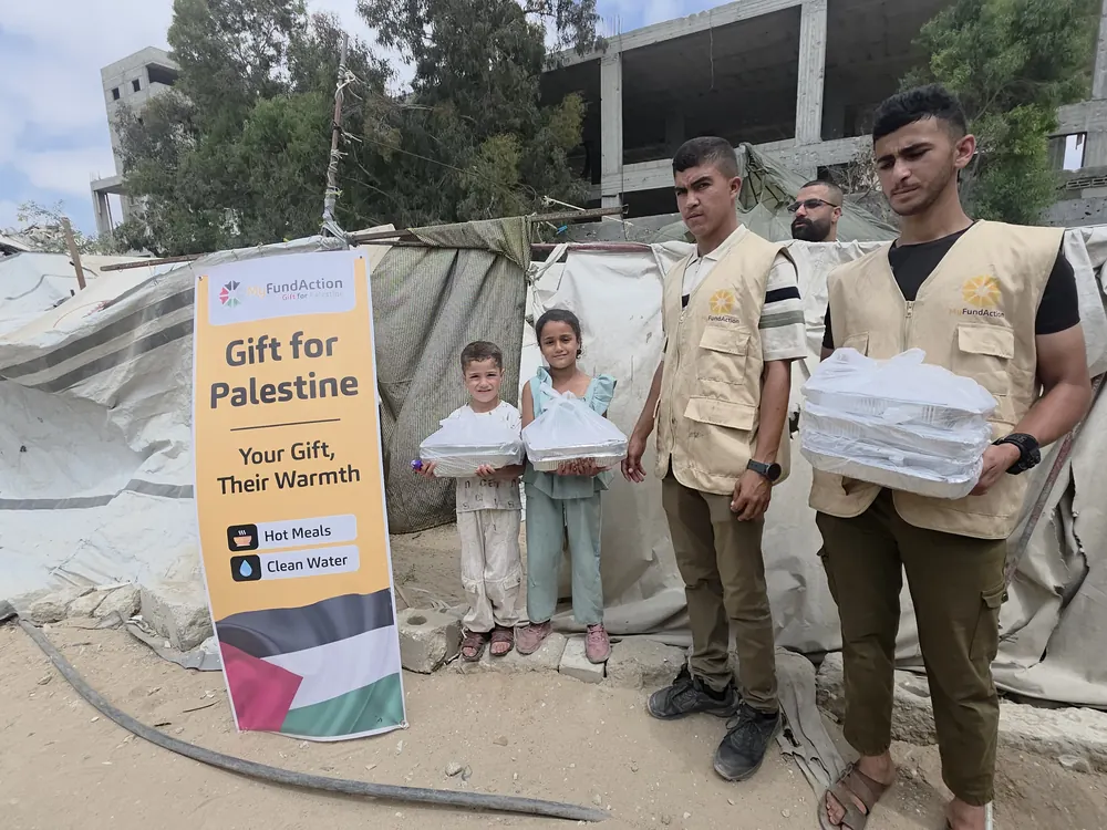 Two children holding packed hot meals beside MyFundAction volunteers at a displacement camp in Gaza