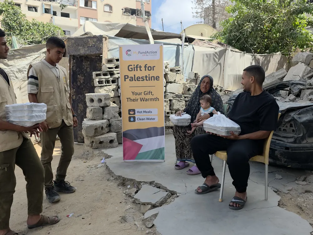 MyFundAction volunteers delivering hot meals to a family sheltering beside a destroyed building in Gaza