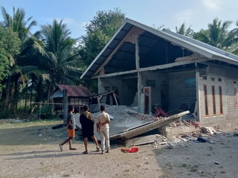 Children walking past a house in Flores with its front wall and veranda brought down by the earthquake