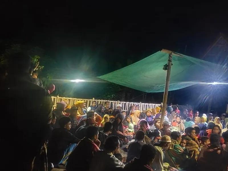 Families gathered under tarpaulins at a displacement site in Flores after dark, lit by temporary lighting