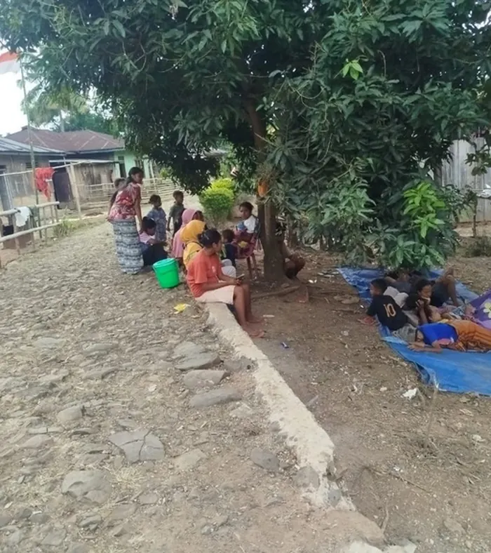 Families sheltering in the open along a village road in Flores, their belongings on tarpaulins spread over bare ground