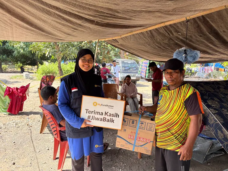 A MyFundAction team member and a young man with a box of supplies and a card reading Terima Kasih #JiwaBaik