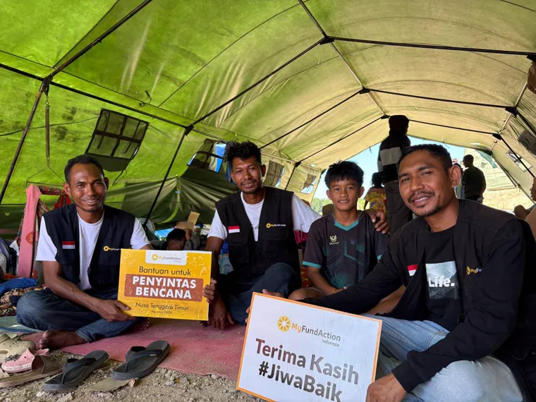 MyFundAction team members and boys inside a shelter tent holding Bantuan untuk Penyintas Bencana and Terima Kasih #JiwaBaik cards
