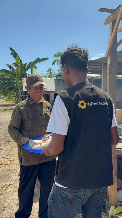 A MyFundAction team member handing a plate of hot food to an older man outside a shelter in Nagekeo