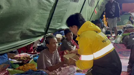 A MyFundAction team member serving a hot meal to an older man in a shelter tent