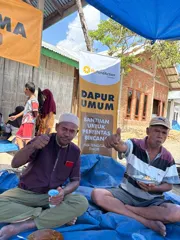 Two men eating a hot meal beneath MyFundAction's Dapur Umum banner